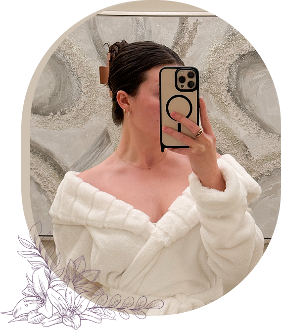 Woman in a white robe taking a mirror selfie with her face partially covered, showcasing a self-care moment at a salon and medspa.
